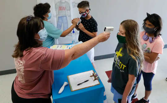 Two teachers standing with masks on checking students for fever with temperatures guns