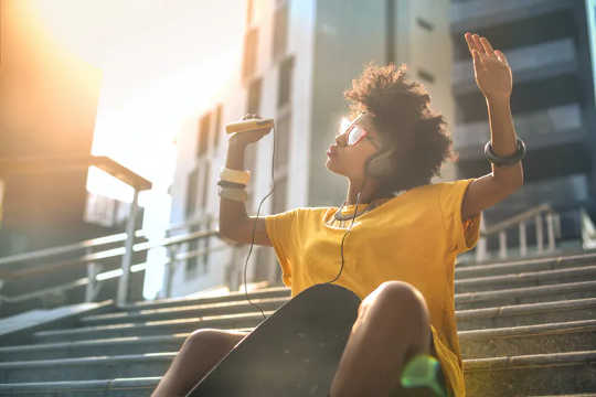 Young woman sitting on the steps, listening to music and waving her arms in the air.