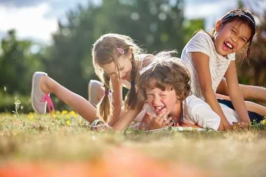 three young children playing on the ground piled up on top of each other