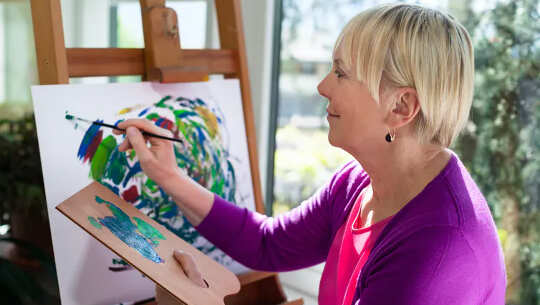 a woman holding a palette and working on a painting 