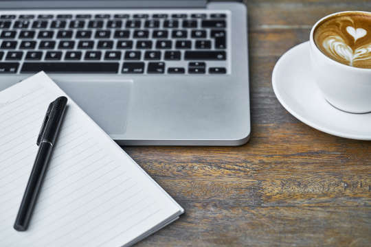 computer keyboard, notebook and pen, and cup of coffee