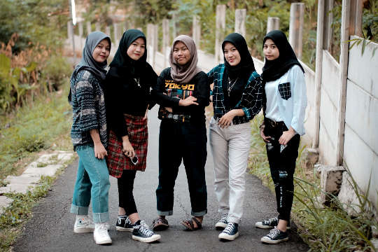 five young women wearing hijabs and dressed in very modern clothing such as jeans