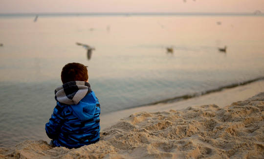 a child sitting on a beach calmly watching flying birds