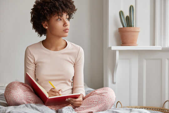 Woman pauses to look out the window while she writes in a notebook.