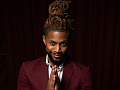 a man, with his dreadlocks tied up in a bun on top of his head, wearing a burgundy suit