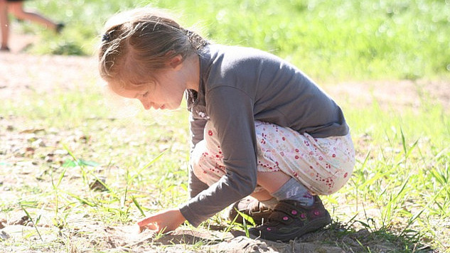 young girl squatting down to the earth and holding a plant