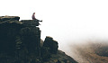 person sitting on the edge of a cliff dangling their legs over the edge