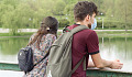 a young couple, wearing protective masks, standing on a bridge