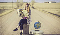 a young woman sitting on a suitcase in the middle of the road with a globe of planet earth next to her