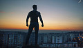 a silhouette of a man with clenched fists standing on a rooftop overlooking the city