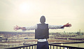 man standing looking out from a balcony with his arms wide open to the horizon