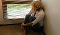 woman sitting on the floor looking out through the cracks of a venetian blinds of a window