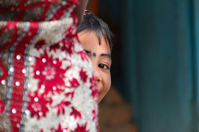 a young East-Indian girl, with a bindi dot or kala tikka on her forehead, and she is peeking out from behind something in a game of hide-and-seek