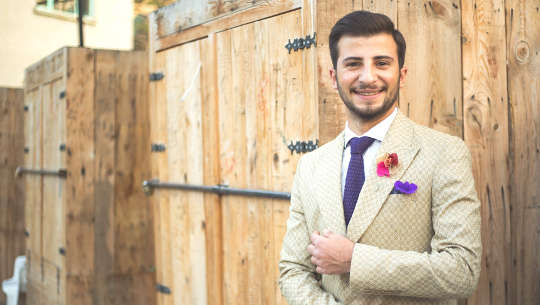 young white man wearing  a suit standing in from of closed doors