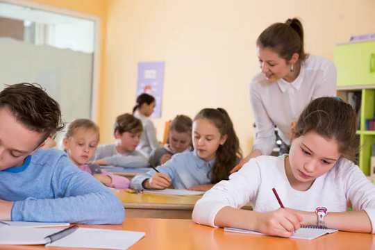 teacher looking on as pupils work in classroom