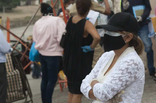 person standing in a crowd and wearing two masks and a hat