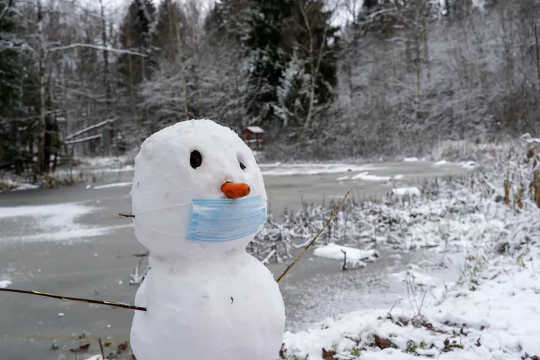 A snowman with a face mask and a carrot nose