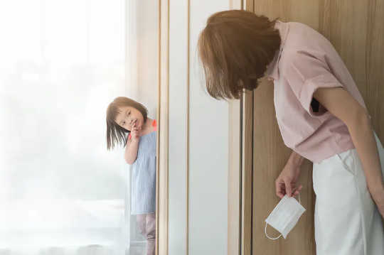 A mother and child playing hide and seek. The mother is holding a mask in her hand. 