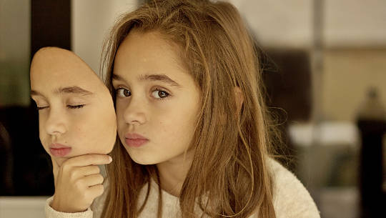 young girl looking sad holding a mask of her own face