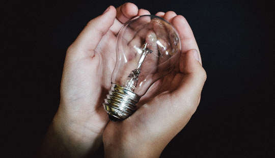 cupped hands holding a light bulb