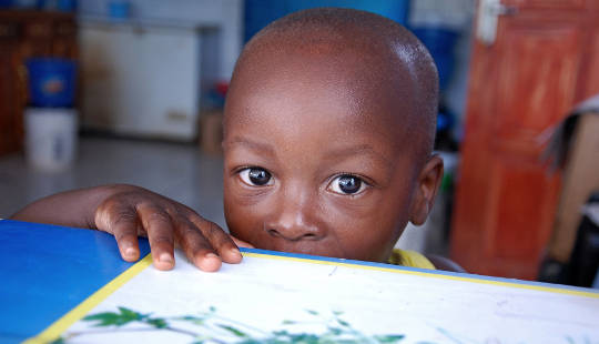 young boy looking out from behind a table