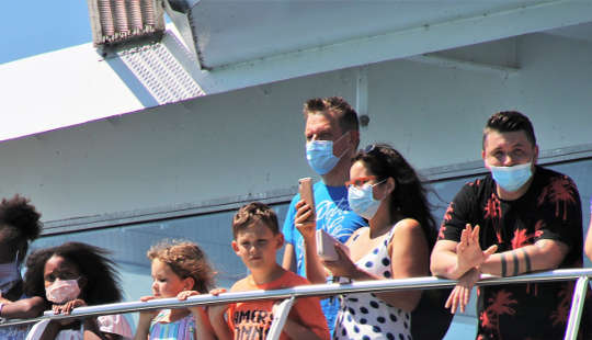 people, most wearing masks, standing on the railing of a cruise ship