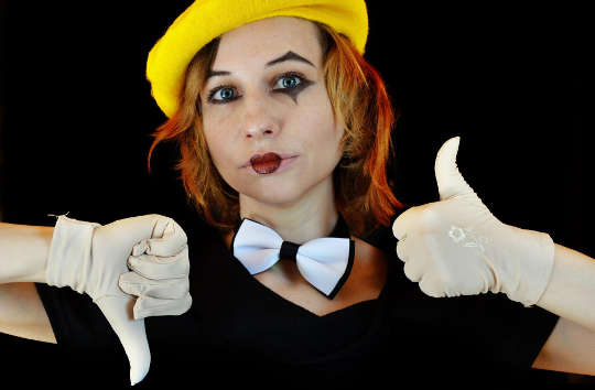 a young woman wearing a bow tie and a clown face with white gloves giving a thumbs up and thumbs down