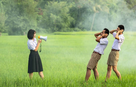 a woman speaking through a megaphone and two men in front of her covering their ears