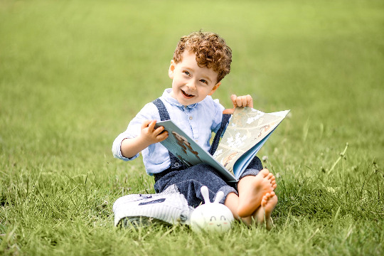 smiling young boy sitting outside with an open book in his hands