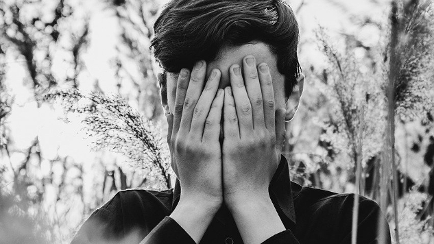 person surrounded by foliage and covering their eyes and face with their hands