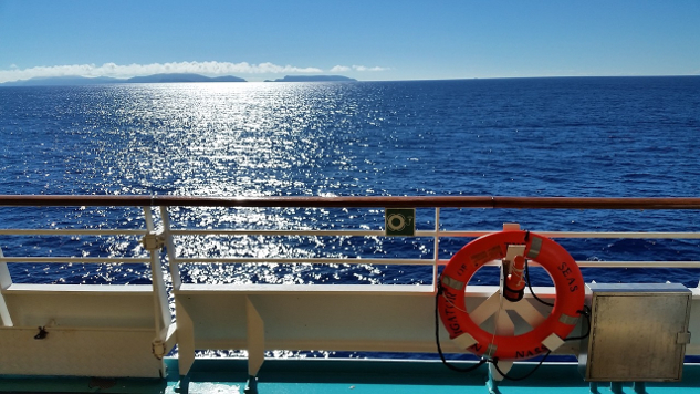 view from the deck of a ship over the water, with a lifesaver on the railing