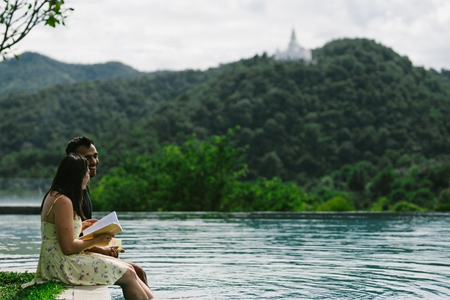 a couple sitting on the edge of a lake reading a book