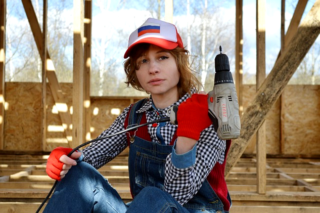 a female construction worker, holding an electric screw-driver pointing up towards the sky