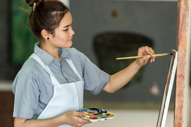 smiling woman paintbrush in hand working on a canvas