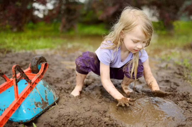 A joyful outdoor scene of children playing in a muddy garden area, hands covered in dirt, with smiles on their faces.