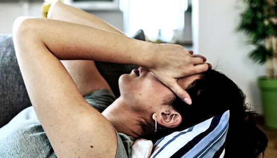 A woman lays down on a couch with her hands over her face