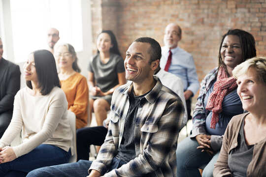 A group of adults in a classroom setting, smiling at the teacher who is out of the frame.