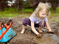 A joyful outdoor scene of children playing in a muddy garden area, hands covered in dirt, with smiles on their faces.