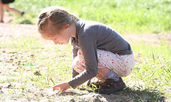 young girl squatting down to the earth and holding a plant