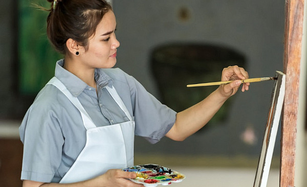 smiling woman paintbrush in hand working on a canvas