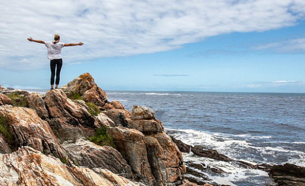 a person standing on rocks overlooking the ocean and the sky with arms wide open