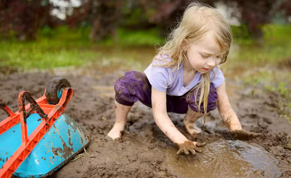 A joyful outdoor scene of children playing in a muddy garden area, hands covered in dirt, with smiles on their faces.