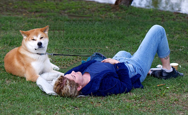 a woman laying back on the grass with her dog