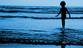 young boy standing in the water at the edge of the waves rippling in