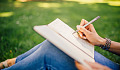 a person sitting outside on the grass writing in a notebook