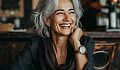 a woman having a cup of coffee radiantly smiling at the person standing in front of her