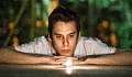 a young man laying down staring into a candle flame