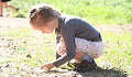 young girl squatting down to the earth and holding a plant